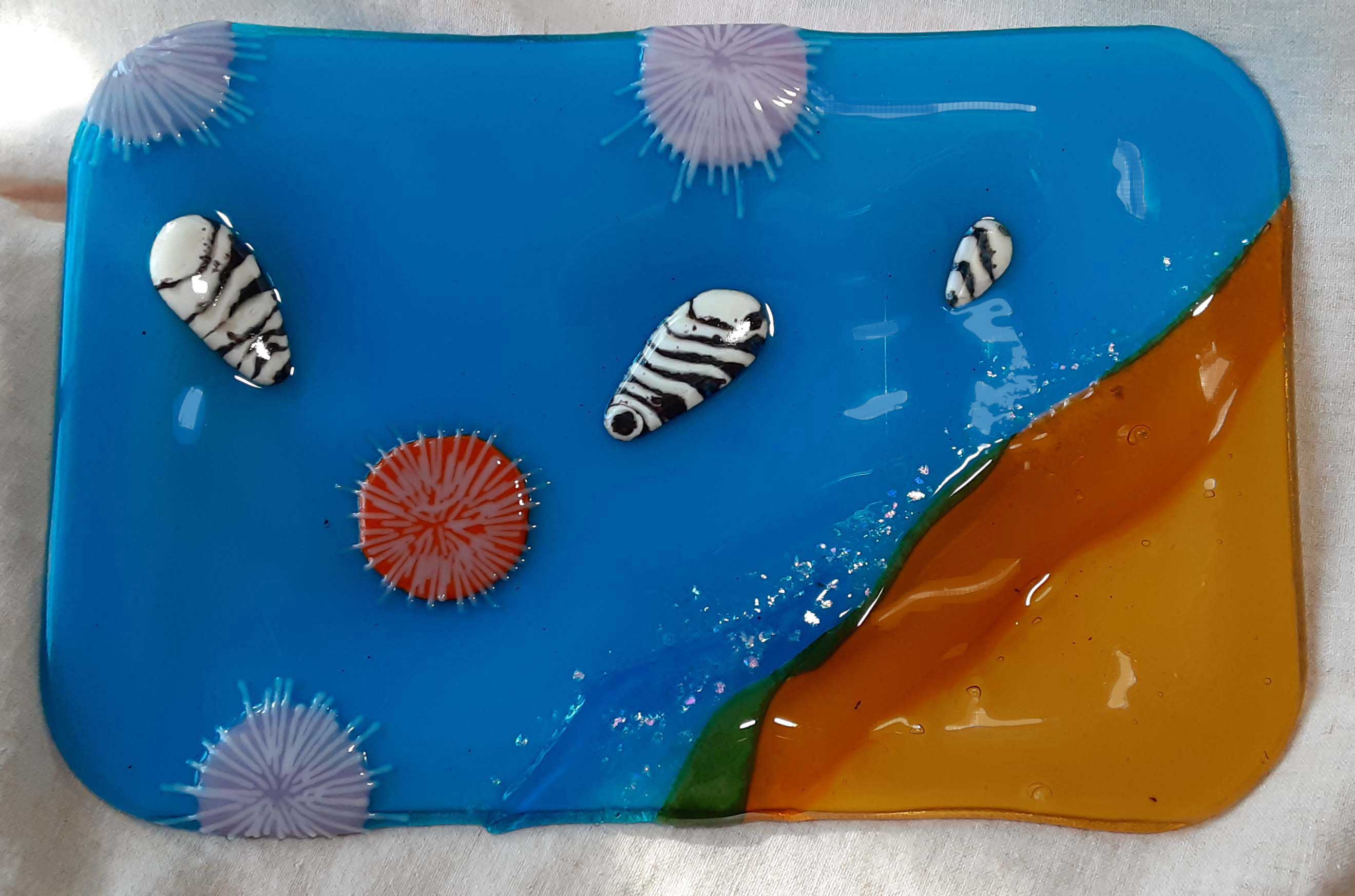 Glass cheese platter with tidal pool colors and sea shells and sea urchins.